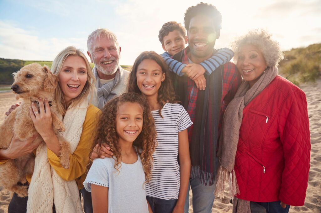 Portrait Of Active Multi-Generation Family On Winter Beach Vacation Resting By Gate